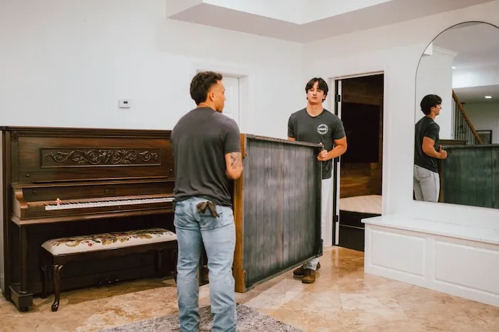 Two junk removal pros carrying furniture from inside a customer's home